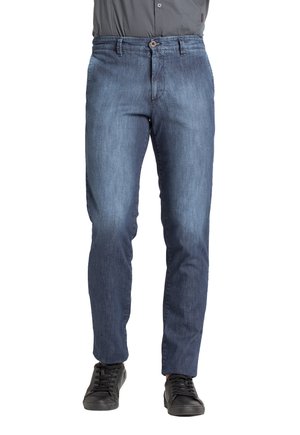 Jeans in denim blu scuro, slim fit, con chiusura a bottone e zip, design a cinque tasche, con sneakers scure sotto.