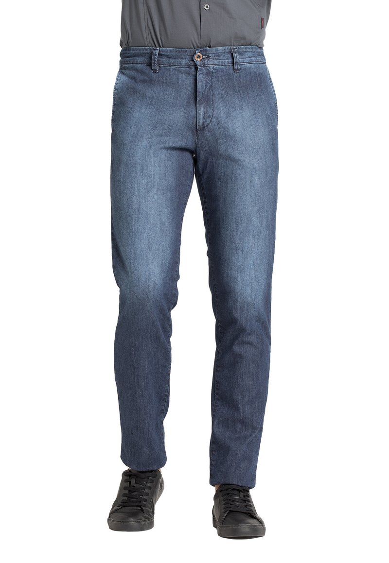 Jeans in denim blu scuro, slim fit, con chiusura a bottone e zip, design a cinque tasche, con sneakers scure sotto.