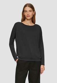 Schwarzes Sweatshirt mit langen Ärmeln aus weichem Stoff, mit verstreuten kleinen Verzierungen und einer lockeren Passform sowie einem weiten Ausschnitt.