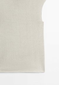 Close-up of the bottom half of a sleeveless beige knitted top on a white background.