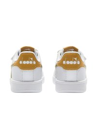 Un paio di sneaker bianche con linguette sul tallone giallo senape marchiate "diadora", viste da dietro su uno sfondo bianco.