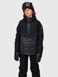 Niño vestido con una chaqueta de esquí negra con patrón de camuflaje, pantalones de esquí negros, guantes negros, un gorro negro y gafas de esquí sobre el casco, frente a un fondo gris.