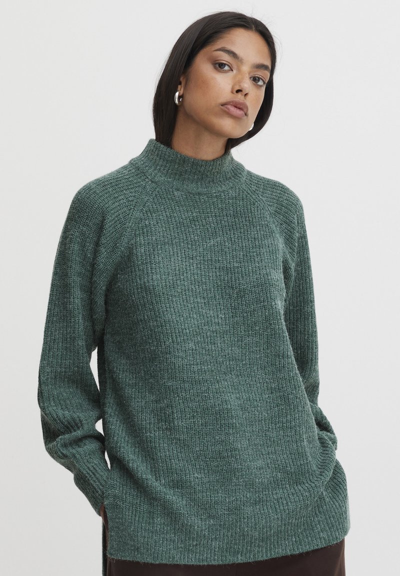 Pull en tricot vert avec un col montant, des manches raglan, un tissu texturé et des fentes sur les côtés à l'ourlet.