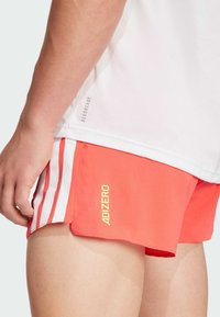 Rode sportieve shorts met witte strepen en een gele "ADIZERO"-logo. Lichtgewicht, ademend materiaal met een licht gestructureerd oppervlak.