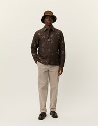 Pruun lillekirjaga särk kraega, beežid sametpüksid ja sobiv pruun müts. Tumedad kingad täiendavad komplekti.