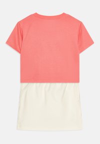 Top corto de color coral con cuello redondo, combinado con una falda fluida color marfil. Textura de tela suave, diseño casual con un aspecto de capas.