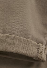 Tissu en coton dans une teinte marron atténuée ; présente une texture côtelée avec un bord effiloché sur l'ourlet pour plus de détail.