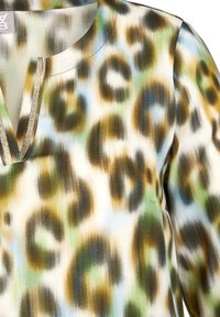Langärmlige Bluse mit einem abstrakten Tierdruck in Grün, Braun und Blau auf einem hellen Hintergrund, mit einem Schlüsselloch-Ausschnitt und subtilem Glanz.