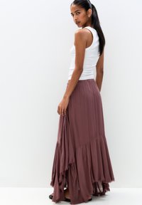 Long, flowing burgundy skirt made of lightweight fabric. Features a tiered design with frayed edges and an elastic waistband.