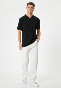 Sort kortærmet skjorte med lynlås-krave, parret med hvide cargo-bukser med sidelommer. Modellen har hvide sneakers på.