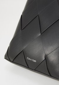 Borsa in pelle nera con un design intrecciato e una superficie liscia, logo "Calvin Klein" impresso nell'angolo in basso a destra.