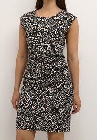 Robe léopard noir et blanc avec des manches courtes, silhouette ajustée, texture lisse, longueur genoux et détails froncés à la taille.