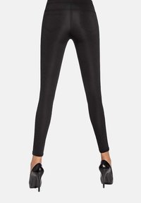 Czarne leginsy z gładkiego, elastycznego materiału, z wysokim stanem i dwiema tylnymi kieszeniami. Noszone z wysokimi obcasami.