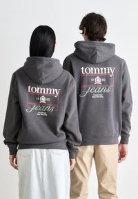 Gray hoodies with "tommy jeans" printed in white and green on the back. Soft fabric, relaxed fit, and ribbed cuffs. Styled with a light skirt.