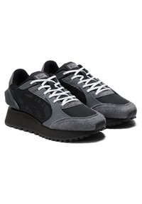 Scarpe sportive nere e grigie caratterizzate da una combinazione di materiali in rete e suede, suola in gomma spessa e lacci bianchi con un motivo testurizzato.