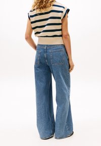 Beżowo-granatowy prążkowany sweter z krótkimi rękawami, zestawiony z jasnoniebieskimi jeansami o szerokich nogawkach, z tylnymi kieszeniami i delikatną fakturą.