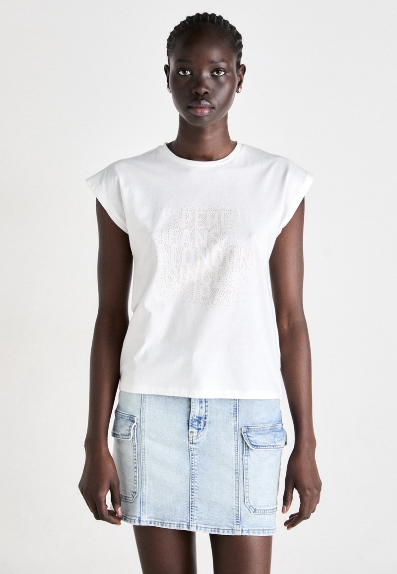 Hvid bomulds t-shirt med korte capærmer, der har et struktureret mærke-logo i beige. Parret med en lyseblå denim mini-nederdel med lommer.
