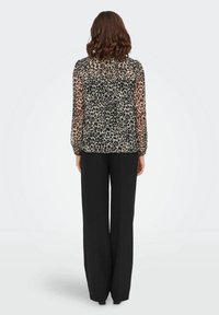 Blusa trasparente con stampa leopardata, maniche lunghe, polsini arricciati e vestibilità comoda, abbinata a pantaloni neri a gamba larga.