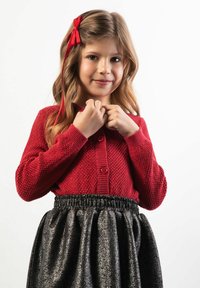 Czerwony sweter na guziki z dzianiny, połączony z falbanianą czarną spódnicą o metalicznym połysku. Charakteryzuje się gładką fakturą i elastycznym pasem.