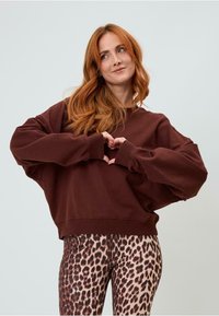 Felpa oversize marrone con spalle scese, polsini a coste e colletto alto, abbinata a leggings aderenti con stampa leopardata.