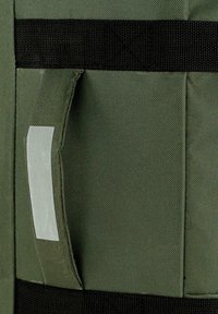 Bolsa de tela verde oliva con correas negras, que cuenta con un bolsillo lateral con un área rectangular para etiqueta. Material texturizado con costuras reforzadas.