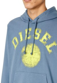 Felpa blu con una stampa grafica gialla che riporta la scritta "DIESEL" e una forma circolare; presenta un cappuccio con cordino e una tasca frontale.