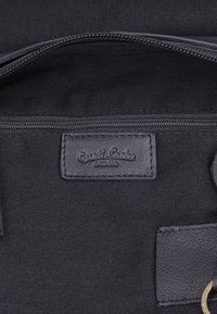 Binnenkant van een zwarte stoffen tas met een leren patch met het logo "Gusti Leder studio" en een rits boven de patch.