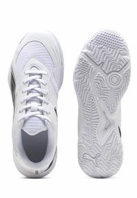 Chaussures de sport blanches avec une tige en mesh, un embout arrondi, des lacets plats, une semelle texturée et un logo noir sur le côté.