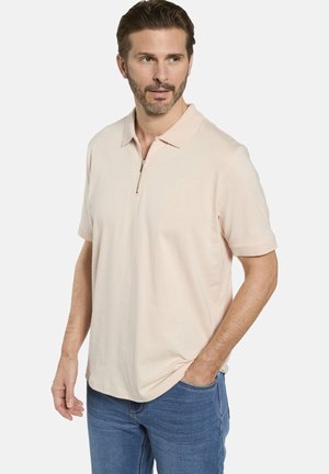 Helles Pfirsichfarbene Polohemd mit einem gerippten Kragen, kurzen Ärmeln und einem halbseitigen Reißverschluss. Getragen mit blauen Jeans. Glatte Textur.