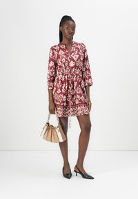 Abito avvolgente a fantasia bordeaux con maniche a tre quarti e vita con cintura, abbinato a una borsa beige e crema e décolleté nere a punta.