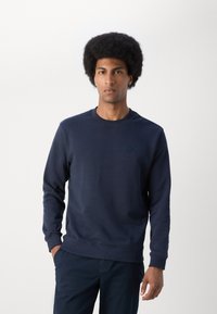 Marineblauwe sweatshirt gemaakt van zachte stof, met een geribde ronde hals en manchetten, en een klein vierkant logo op de borst.
