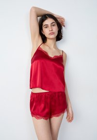 Rode satijnen slaapset met een cami-top met kanten rand en bijpassende short. Gladde textuur, losse pasvorm en gegolfde randen.