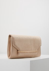 Clutch bag in suede beige con una forma strutturata, caratterizzata da un accento in hardware dorato e una chiusura a patta. Texture liscia e design minimalista.