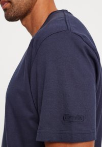 Navy blue cotton t-shirt with short sleeves, featuring a round neckline and subtle branding on the left sleeve. Smooth texture.