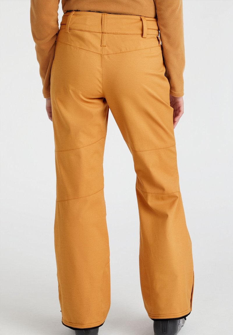 Pomarańczowe spodnie narciarskie o luźnym kroju, z wzmocnionymi szwami, zamkami błyskawicznymi u kostek i gładkim, teksturowanym materiałem.