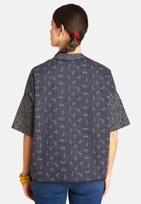 Kurzärmliges Oberteil aus dunkelblauem Stoff mit geometrischem Muster, kontrastierenden gemusterten Ärmeln und kragen.