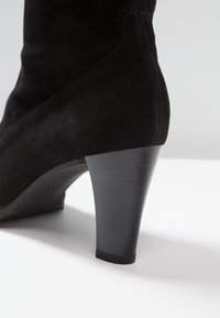 Bottine en daim noir avec un talon effilé, une texture lisse, des coutures renforcées et une légère brillance.