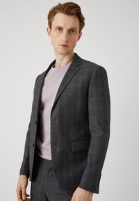 Grå rutete blazer med stikklapper, enkelt knappelukking og frontlommer, kombinert med en lys rosa t-skjorte. Glatt stofftekstur.