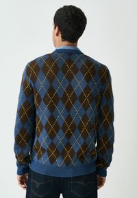 Pullover mit Argyle-Muster in Braun und Blau mit gelben Akzenten; verfügt über einen gerippten Kragen und Ärmelbündchen; gestrickte Textur.