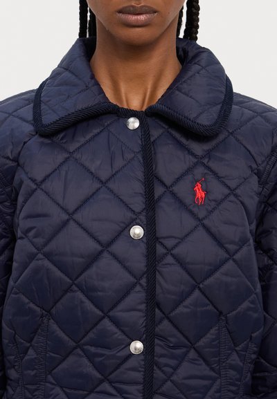 Jūras spēku kviltota jaka ar lielu apkakli, sudraba poga un izšūtu sarkanu nozīmīti. Iespējas ar dimanta formas šuvēm un gludu tekstūru.