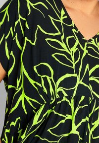 Top di tessuto nero con scollatura a V, caratterizzato da audaci motivi a foglia color verde lime e un design a vita ampia e arricciata. Materiale leggero e textured.