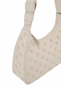 Sac à main beige de forme arrondie, en simili cuir texturé, décoré de clous dorés régulièrement espacés, avec une fermeture zippée en haut.