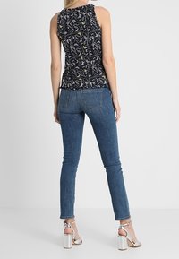 Top senza maniche nero con motivo a fantasia e design floreale multicolore, abbinato a jeans skinny blu e sandali con tacco alto argentati.