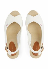 Sandalias de cuña blancas de lona con un diseño entrecruzado, forro de tela color marrón y un acento en hebilla marrón. La suela presenta un patrón texturizado.