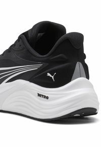 Chaussure de sport noire avec une tige en textile lisse, des accents blancs et gris, une semelle blanche rembourrée et un logo discret sur le côté.