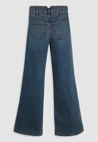 Jeans de ganga azul com corte amplo e cintura alta, com dois bolsos traseiros e costura visível. Textura suave com desbotamento mínimo.