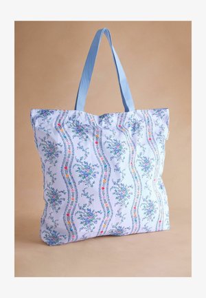 Kék virágmintás vászontáska, színes virágokkal és indákkal, semleges barna háttérrel.