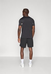 Svart tränings t-shirt med texturerade ärmar, kombinerad med svarta shorts. Tillbehören inkluderar vita strumpor och ljusa sneakers.