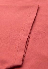 Bavlněná tkanina v tlumené korálové barvě s hladkým povrchem. Vyznačuje se plochým šitím podél okrajů, což zdůrazňuje čisté designové linie.