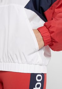 Röd, vit och marinblå färgblockerad jacka; elastiska ärmslut; sidofickor; mjuk textur; fåll drar ihop sig för en figursydd look.